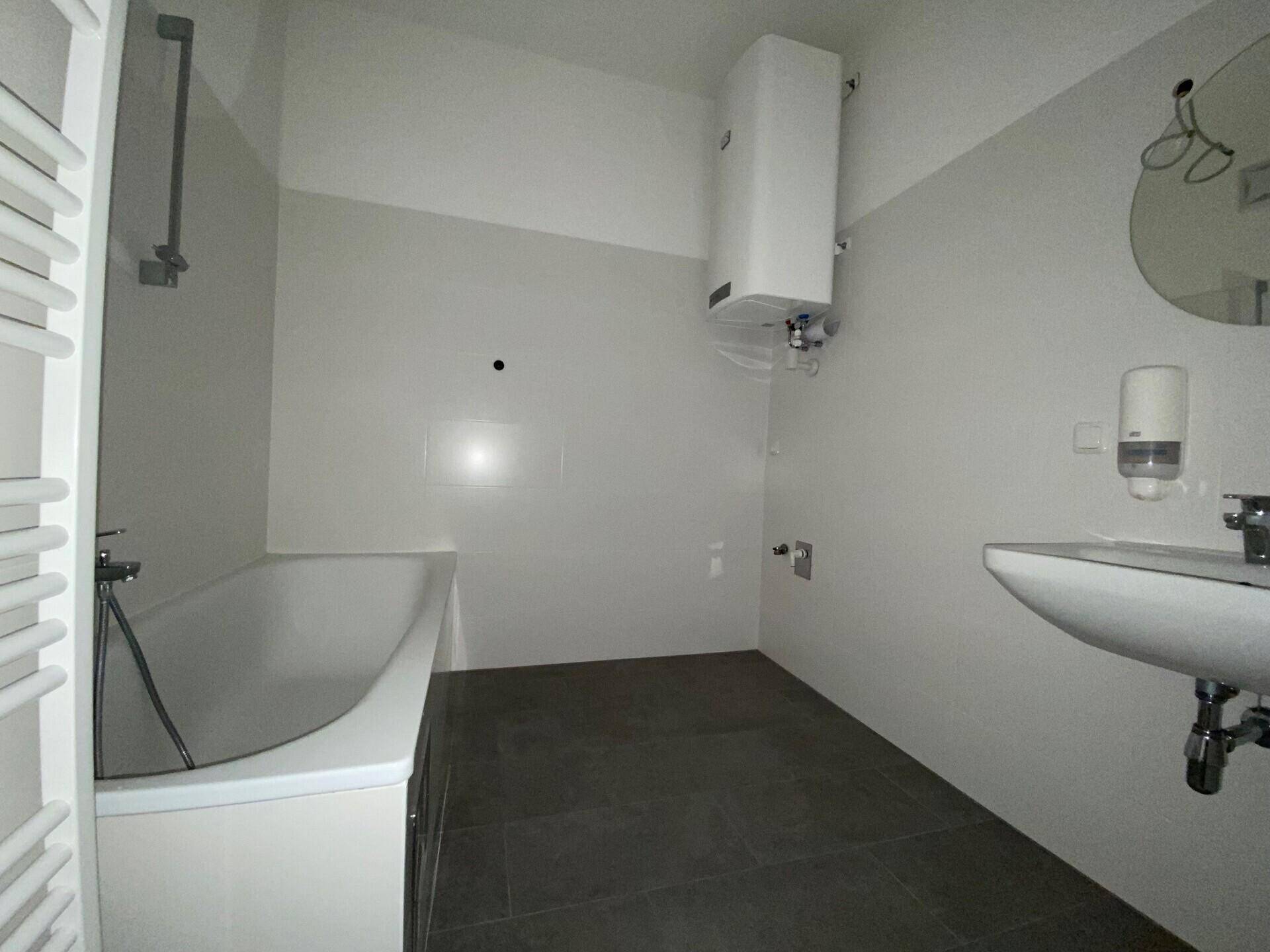 Badezimmer mit Badewanne, Waschbecken, Wandspiegel und einem Warmwasserboiler an der Wand.