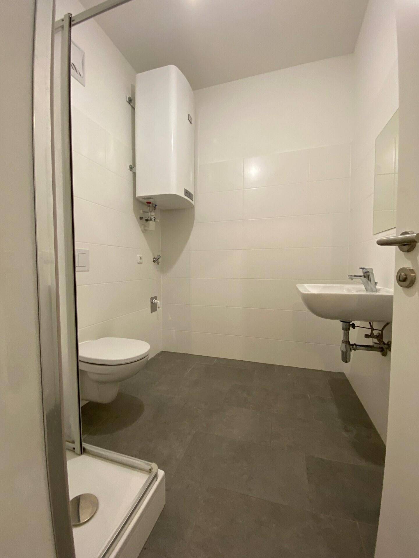 Modernes Badezimmer mit grauen Fliesen, weißer Wandverkleidung, Dusche, WC und Waschbecken.