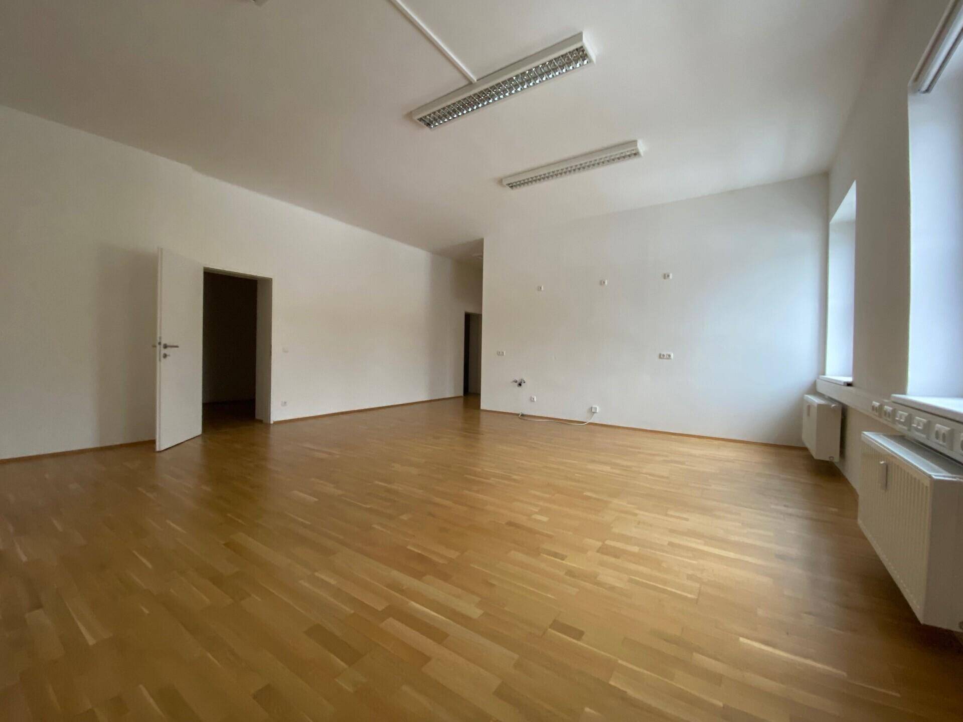 Großer, leerer Büroraum mit Parkettboden und mehreren Türen, bereit für die individuelle Gestaltung.