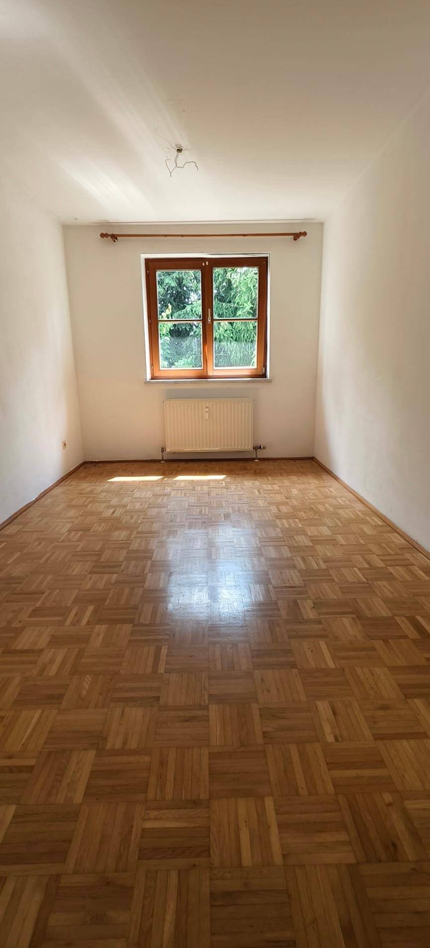 Heller Raum mit Parkettboden und einem Fenster, das viel Tageslicht hereinlässt.