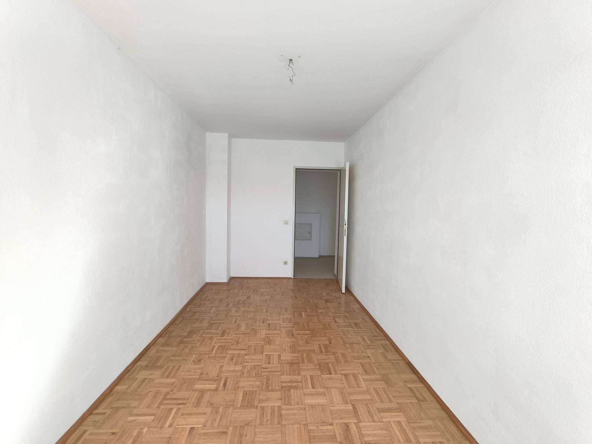 Leerer Raum mit hellem Parkettboden und weißen Wänden, bereit zur individuellen Gestaltung.