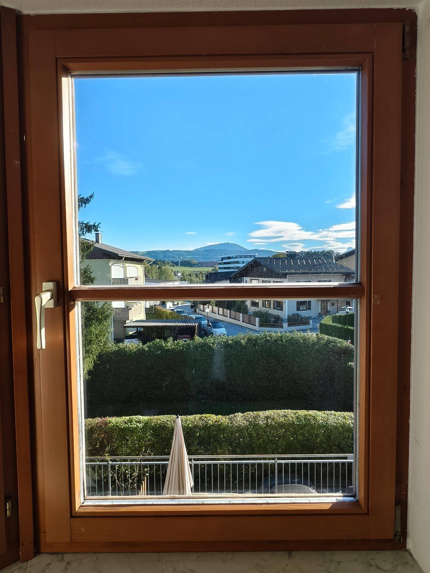 Blick aus einem Fenster mit Holzrahmen auf eine Berglandschaft und umliegende Häuser.