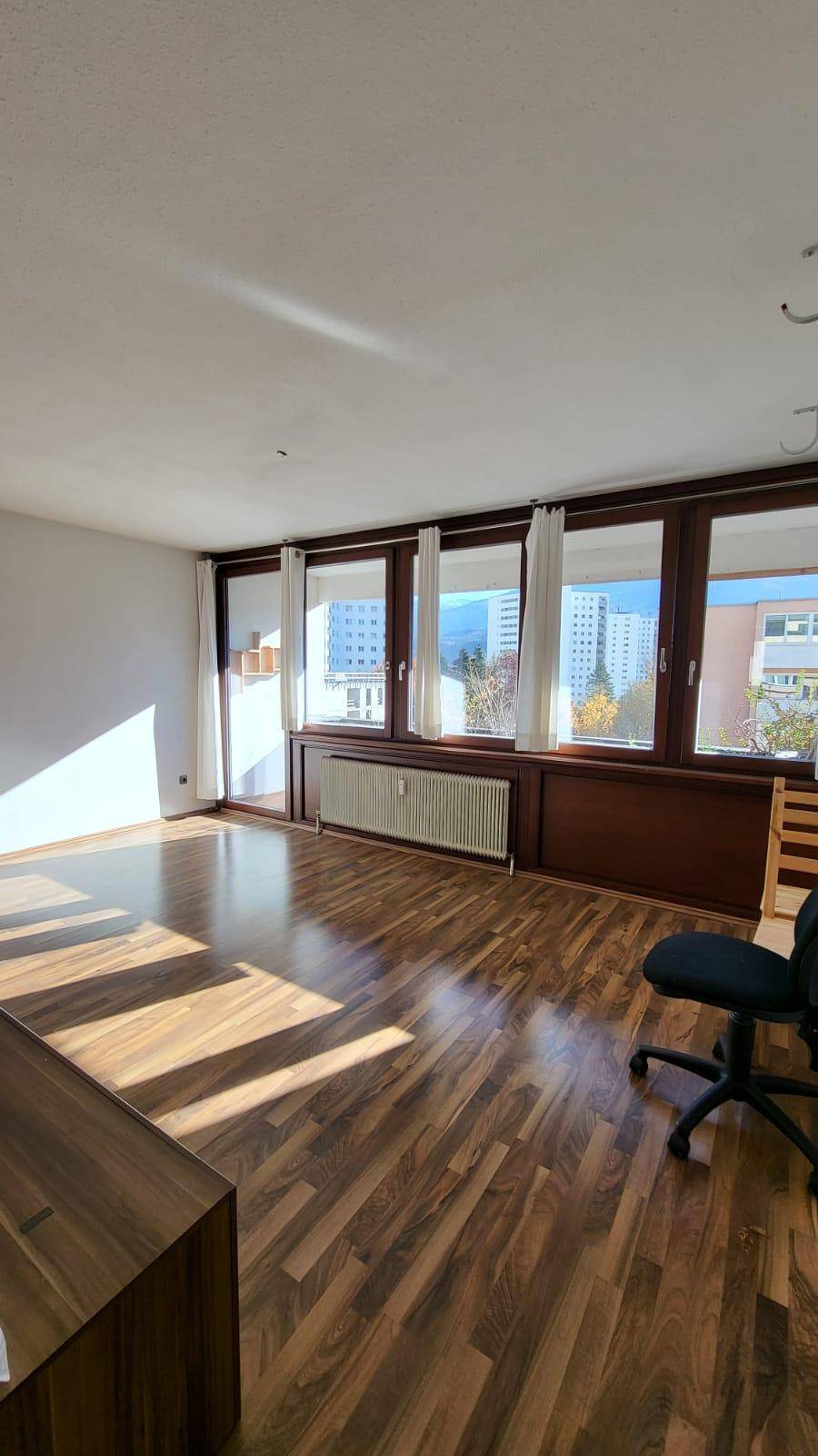Geräumiger Wohnbereich mit Holzboden, großen Fenstern und viel natürlichem Licht.