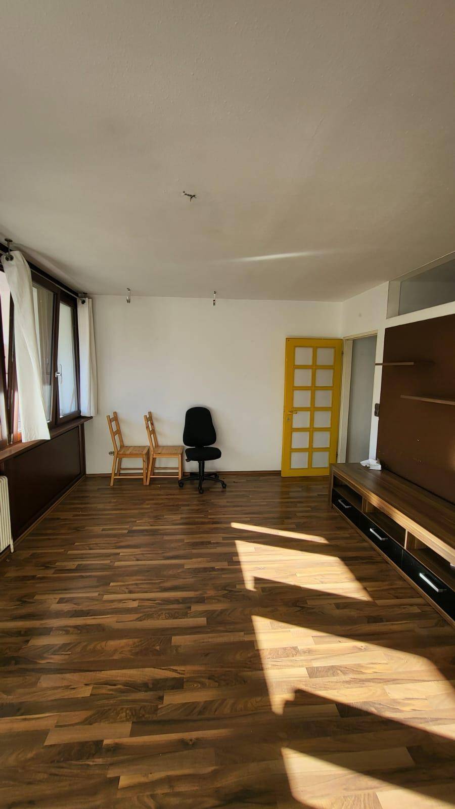 Heller Wohnraum mit Holzboden, großen Fenstern und einer auffälligen gelben Tür.