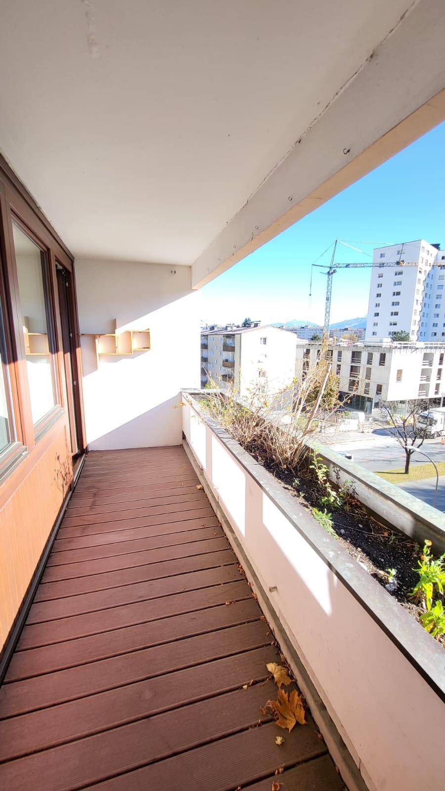 Langer Balkon mit Holzboden und Blick auf die Stadt und umliegende Gebäude.