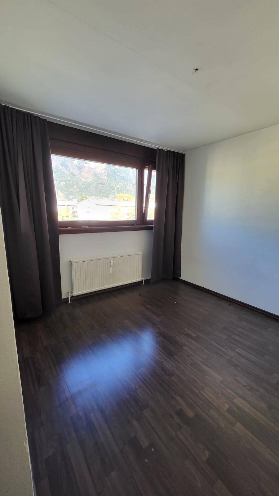 Schlafzimmer mit Holzboden, großem Fenster und dunklen Vorhängen für Privatsphäre.