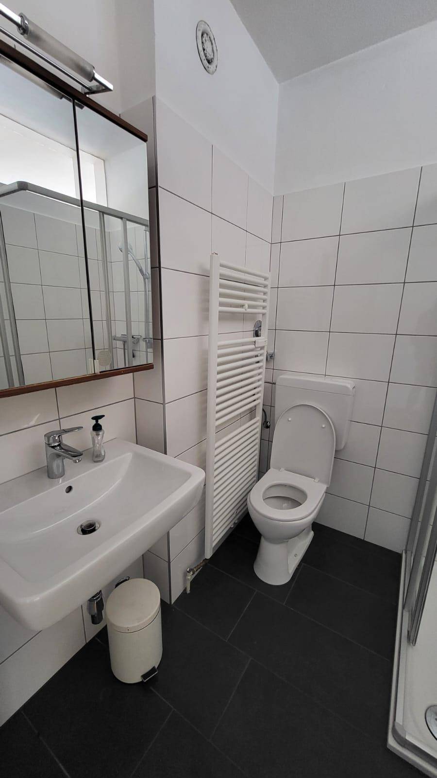 Modernes Badezimmer mit weißen Wandfliesen, dunklem Boden und beheiztem Handtuchhalter.