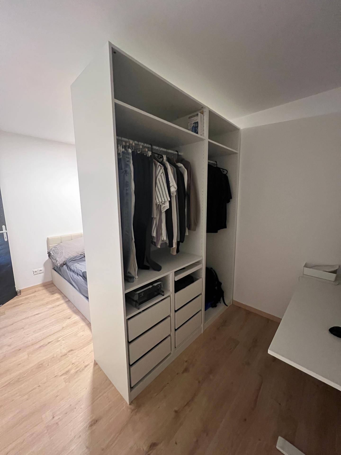 Schlafzimmer mit offenem Kleiderschrank und Stauraum, der als Raumteiler dient.