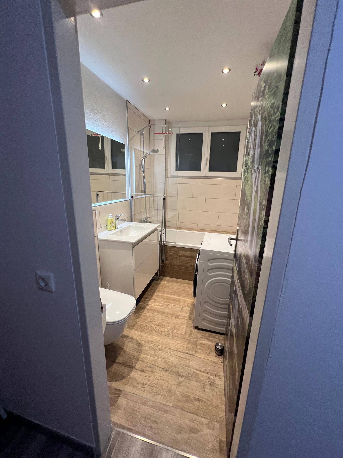 Modernes Badezimmer mit Toilette, Waschbecken, Badewanne und Waschmaschine.