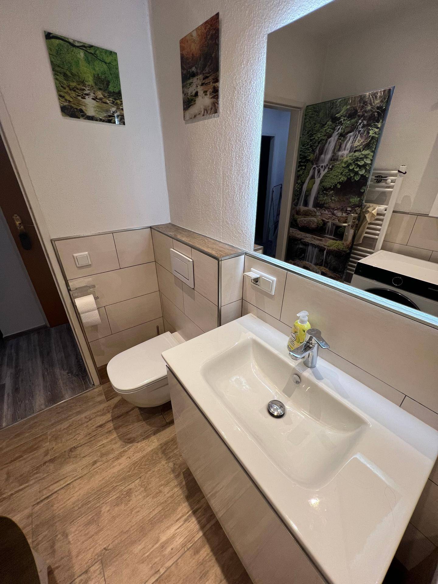 Detailansicht des Waschbeckens und der Toilette im modernen Badezimmer mit großem Spiegel.