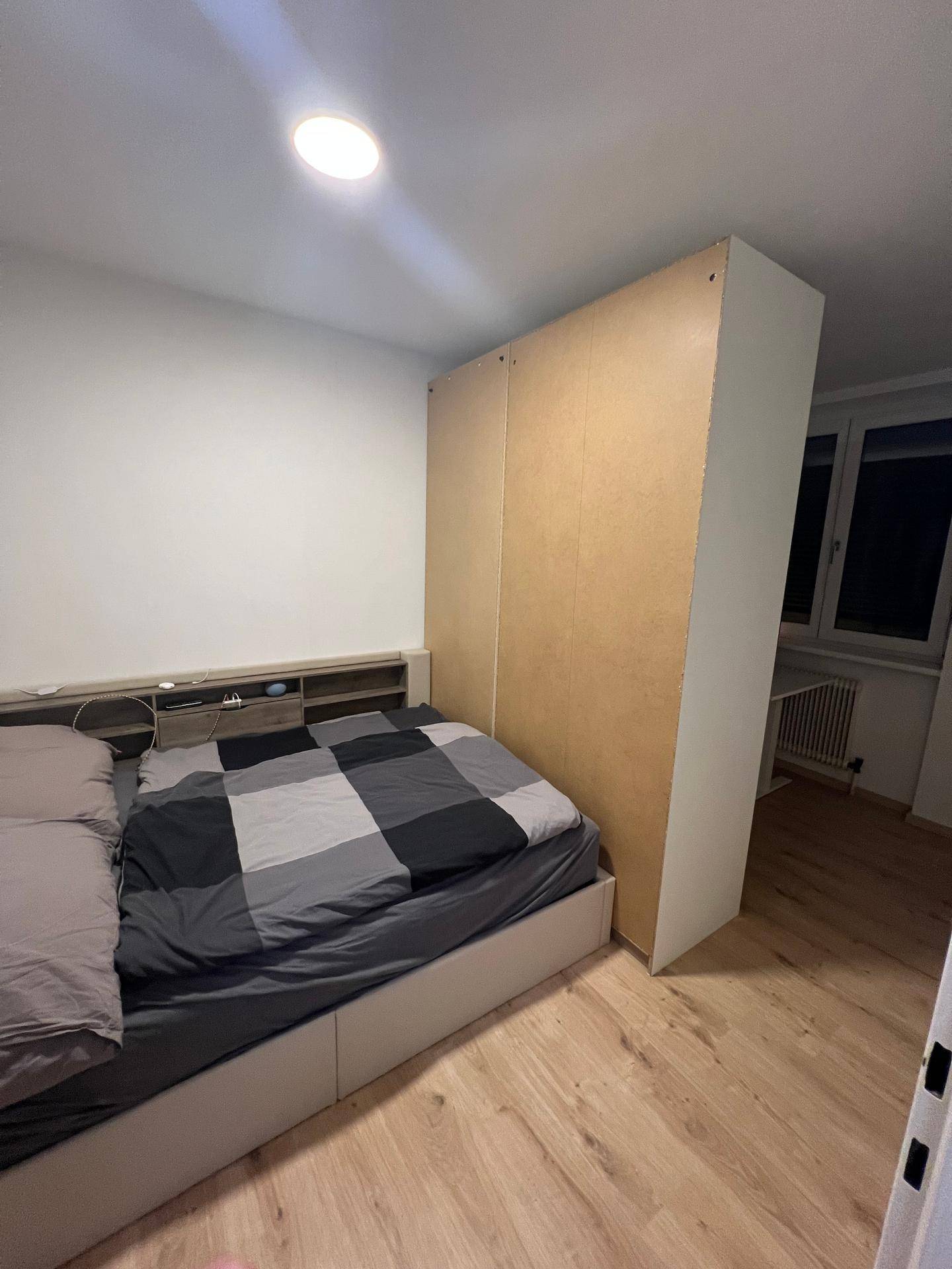 Schlafzimmer mit Bett, integriertem Kopfteil und einem hohen Kleiderschrank als Raumteiler.