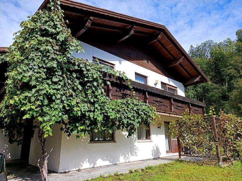 Hausfassade mit traditionellem Holzbalkon und üppiger Begrünung im Vordergrund.