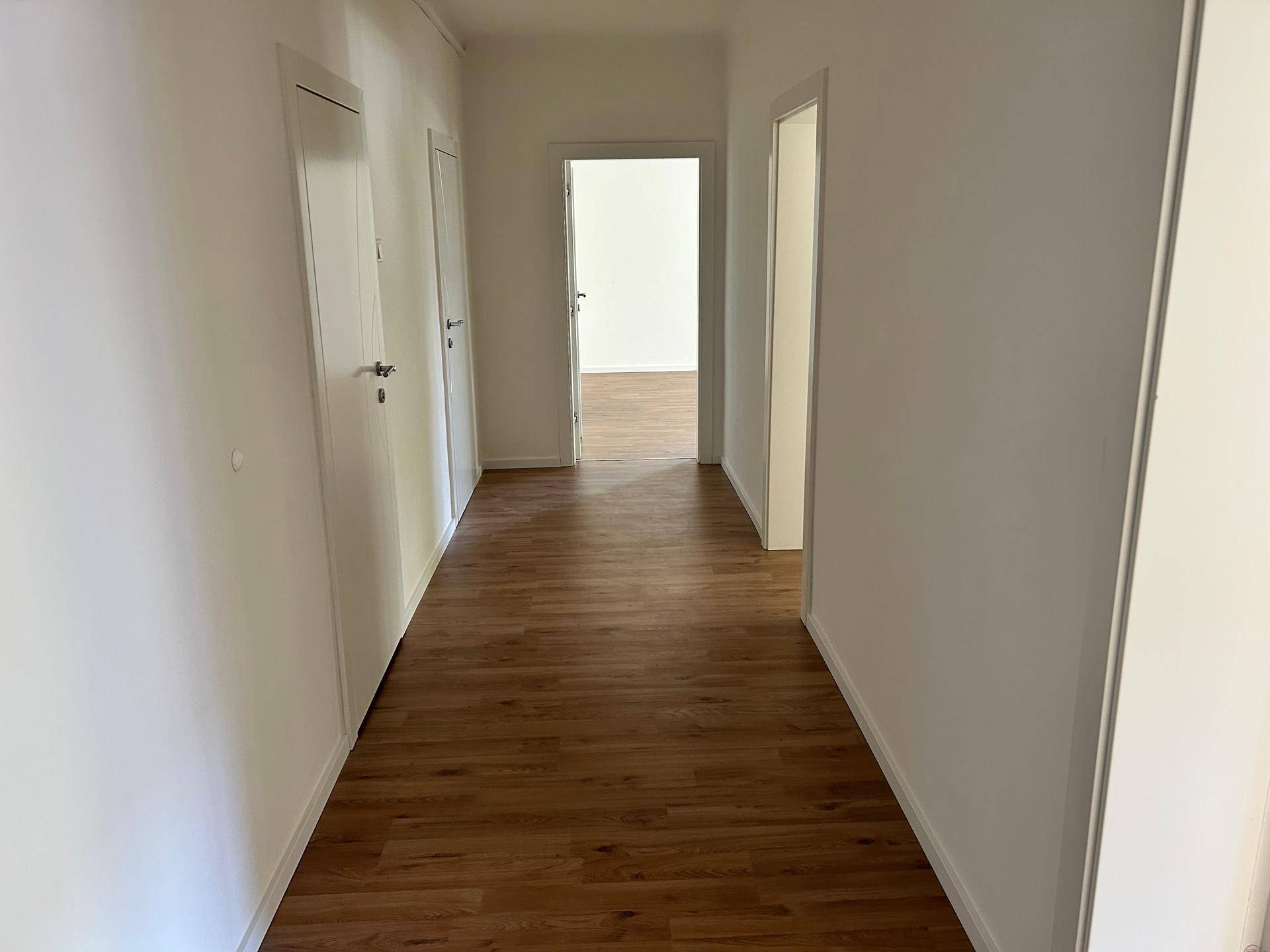Heller Flur mit Laminatboden und mehreren weißen Türen, die zu den angrenzenden Räumen führen.