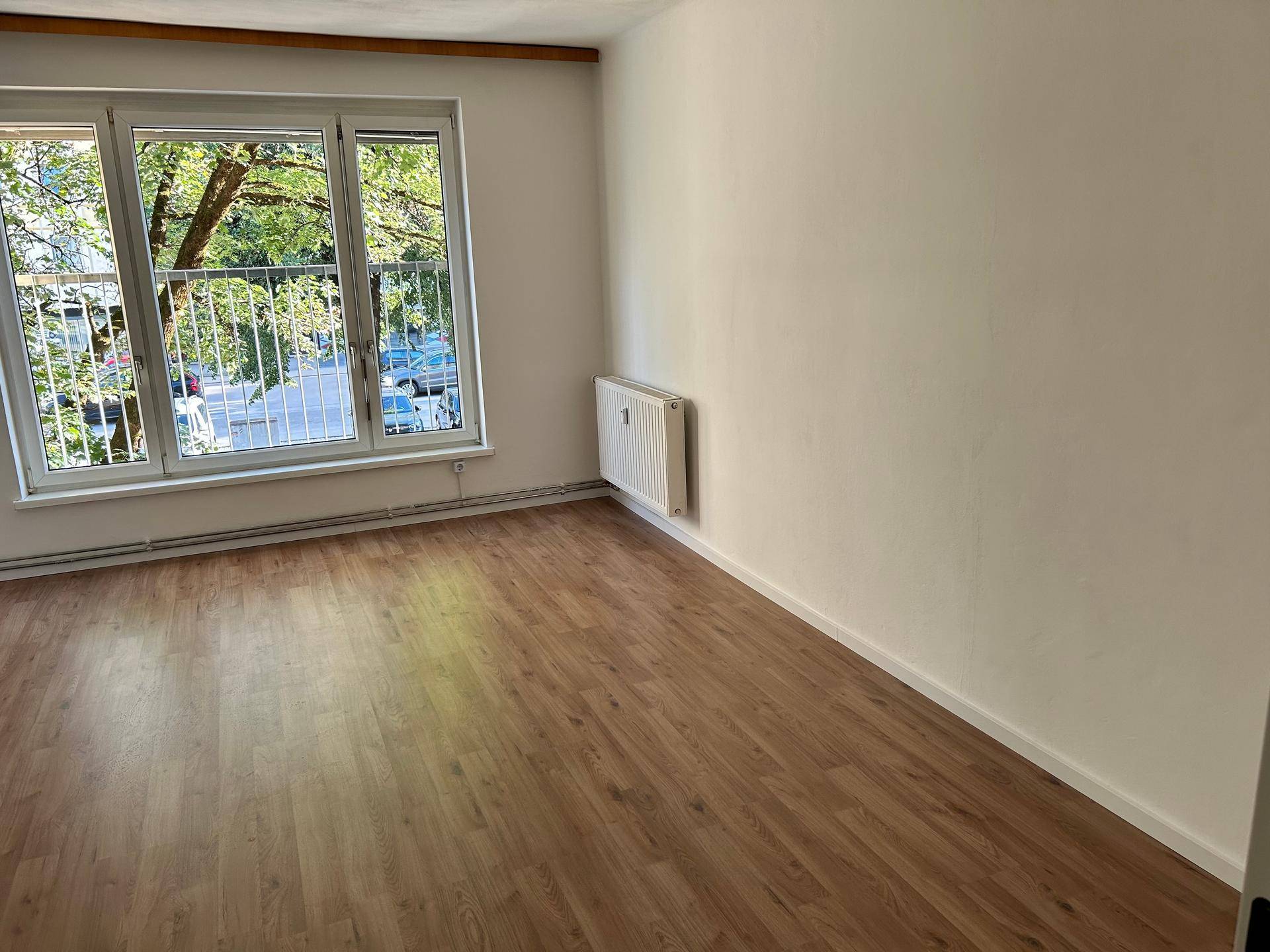 Freundliches Zimmer mit Laminatboden und großem Fenster, das viel Tageslicht hereinlässt.