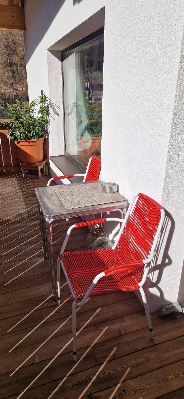 Sonniger Außenbereich mit Holzboden und roten Gartenstühlen, ideal zum Entspannen.
