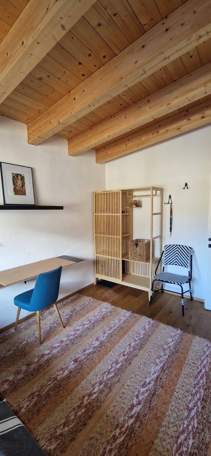 Schlafzimmer mit Holzbalkendecke, Teppich und offenem Kleiderschrank, der viel Stauraum bietet.