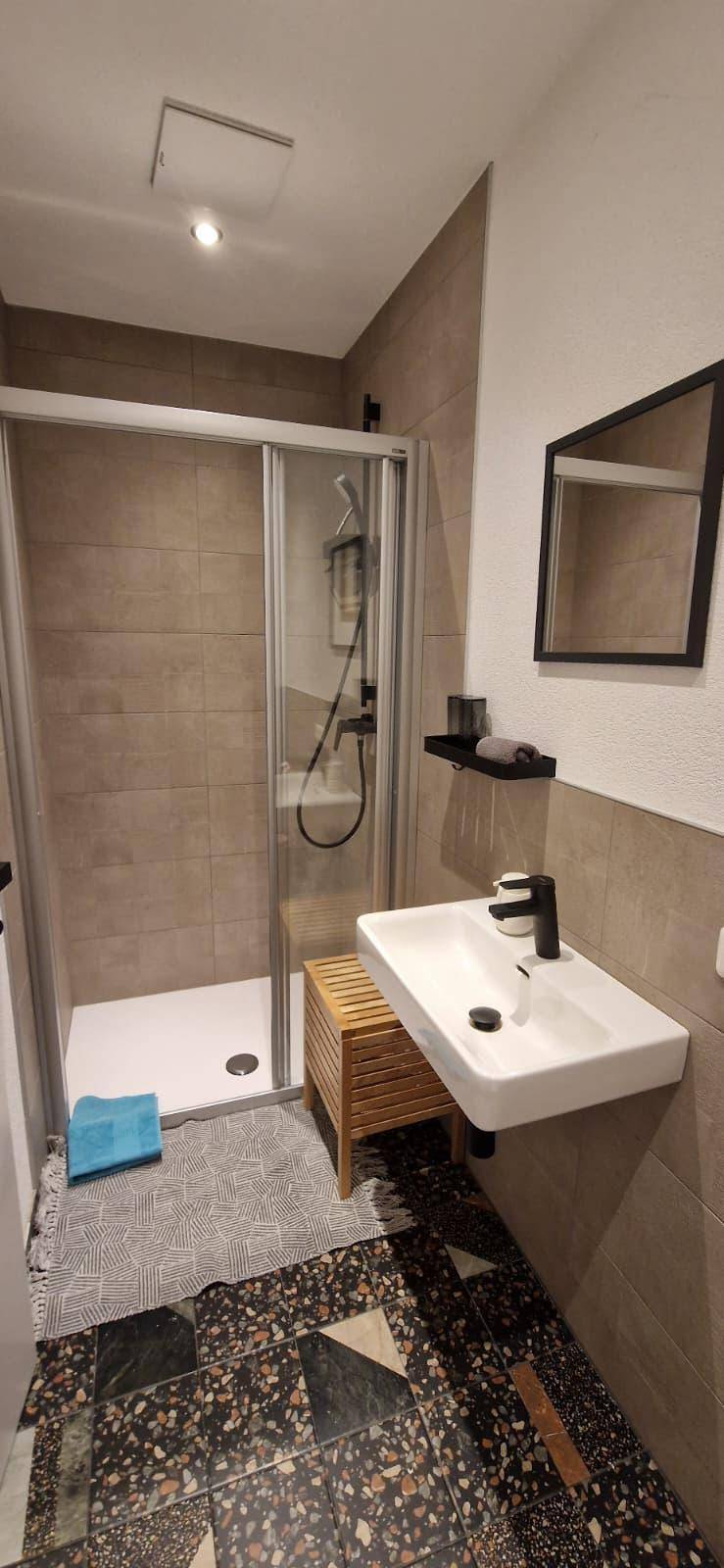Modernes Badezimmer mit Duschkabine, Waschbecken und dunklen Fliesen am Boden.