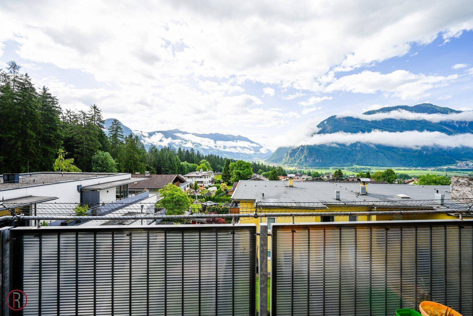 Panoramablick von einem Balkon auf die umliegende Berglandschaft und bewölkten Himmel.