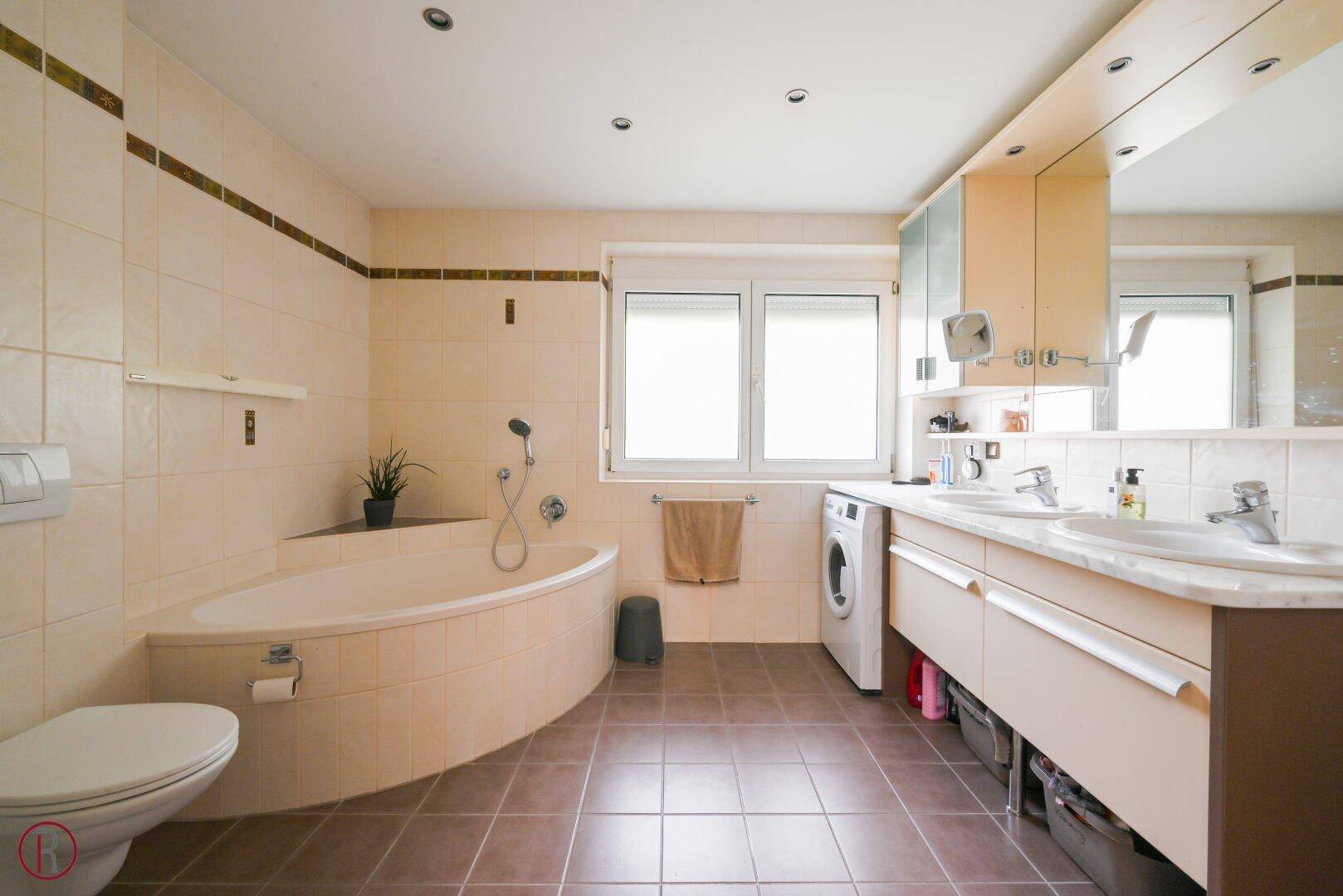 Helles Badezimmer mit Badewanne, Dusche, Doppelwaschbecken und integrierter Waschmaschine.
