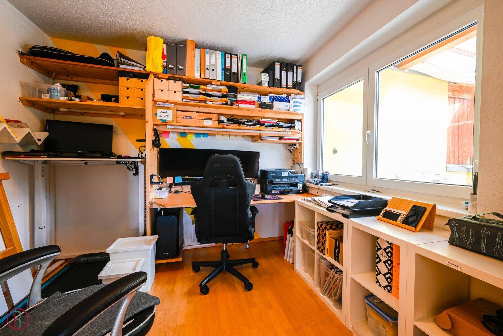 Funktionales Heimbüro mit Schreibtisch, Regalen und viel Stauraum, gut beleuchtet durch ein Fenster.