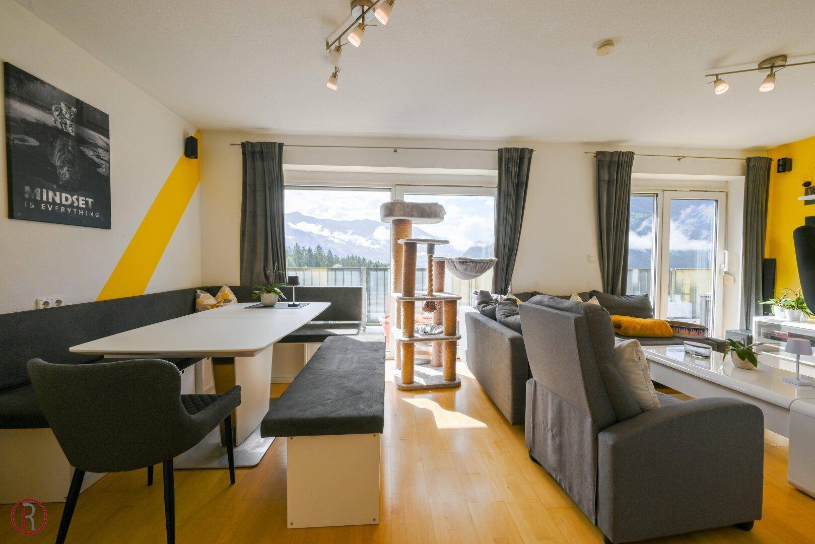 Heller Wohn-Essbereich mit Holzboden, gemütlicher Sitzecke und weitem Bergblick durch große Fenster.