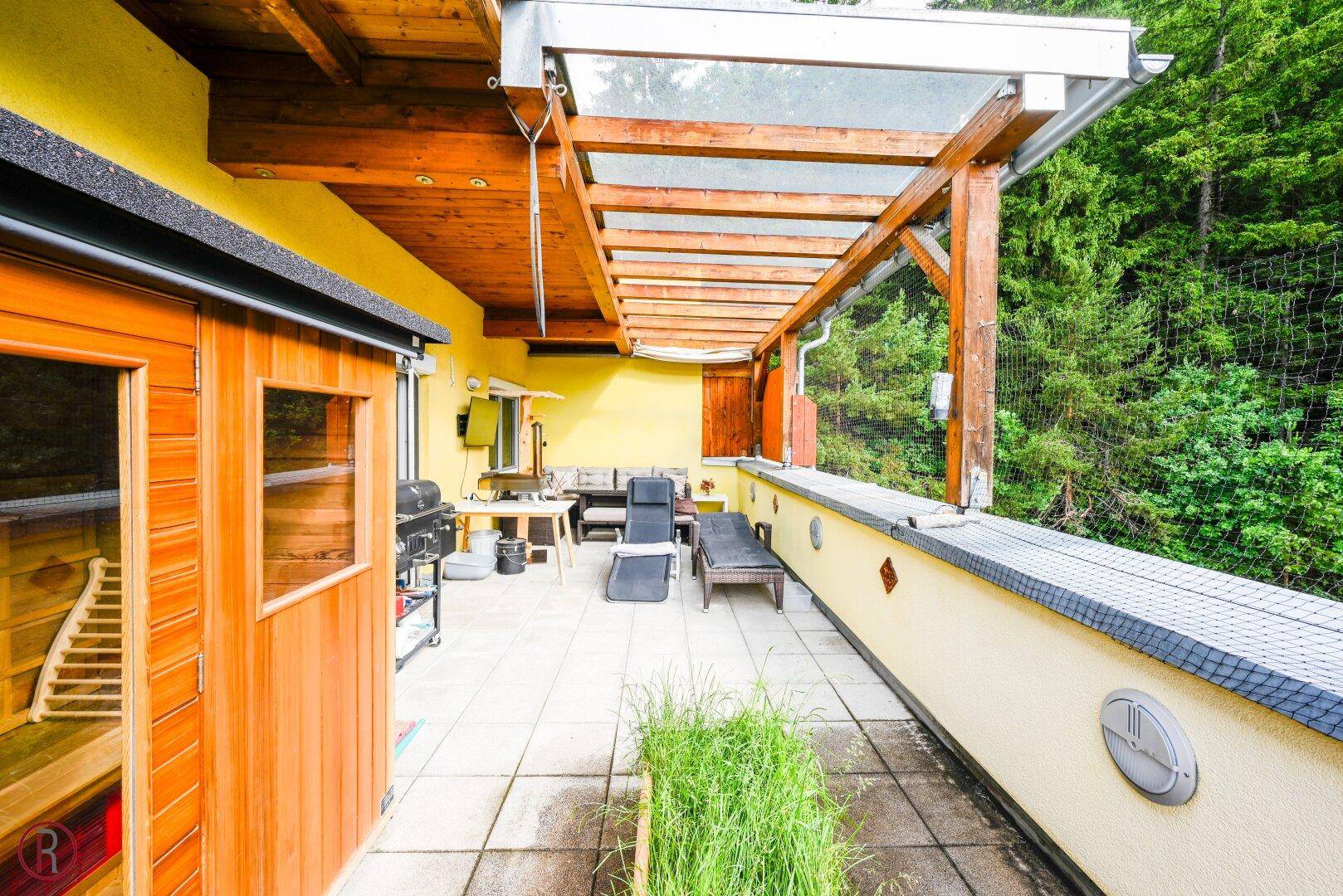 Geräumige überdachte Terrasse mit integrierter Sauna und Blick ins Grüne, ideal zum Entspannen.