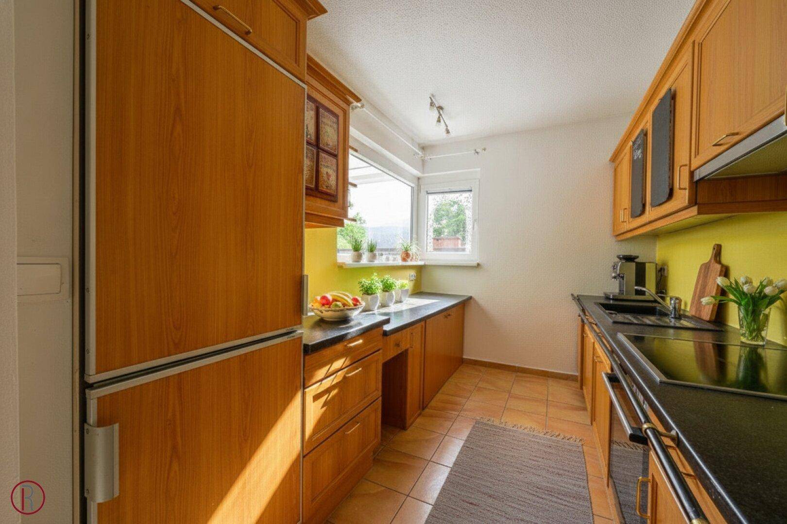 Funktionale Küche mit Holzschränken, dunkler Arbeitsplatte und Fenster mit Blick ins Freie.