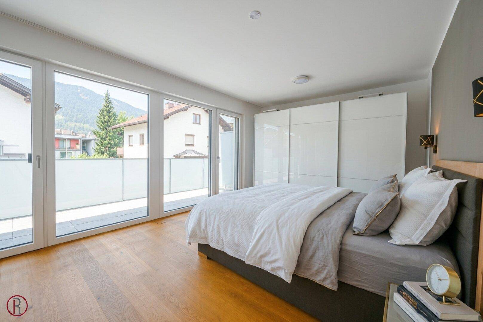 Helles Schlafzimmer mit Holzboden, großen Schiebetüren zum Balkon und einem geräumigen Kleiderschrank.