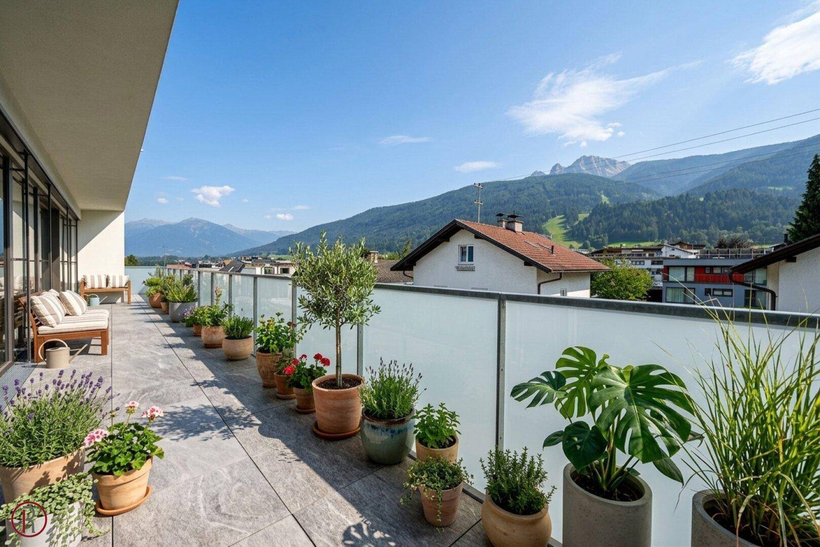 Lange, sonnige Terrasse mit zahlreichen Pflanzen und einem weiten Blick auf die umliegende Berglandschaft.