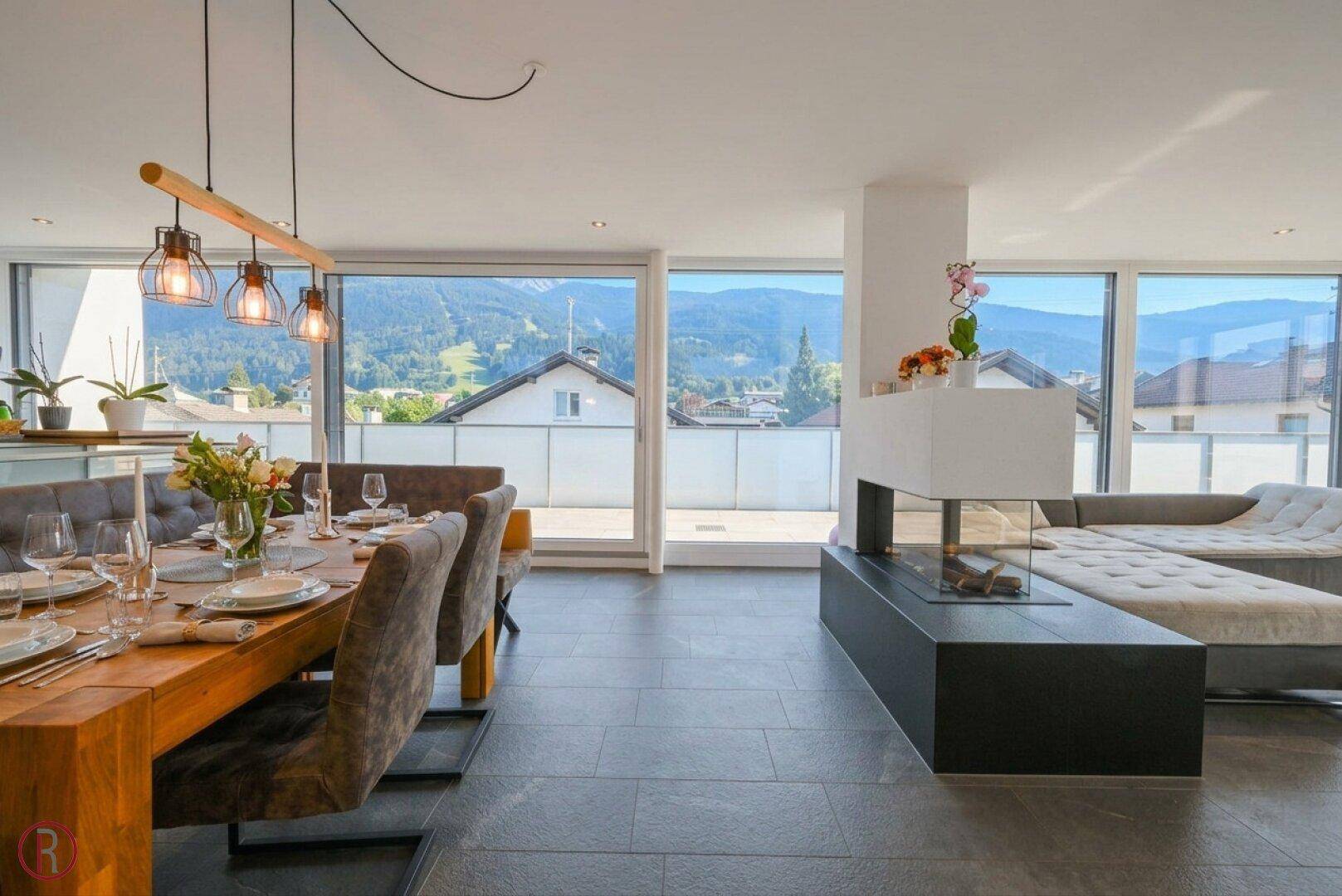 Gemütlicher Essbereich mit Holztisch und Blick auf die Berge, verbunden mit einem modernen Wohnbereich und Kamin.