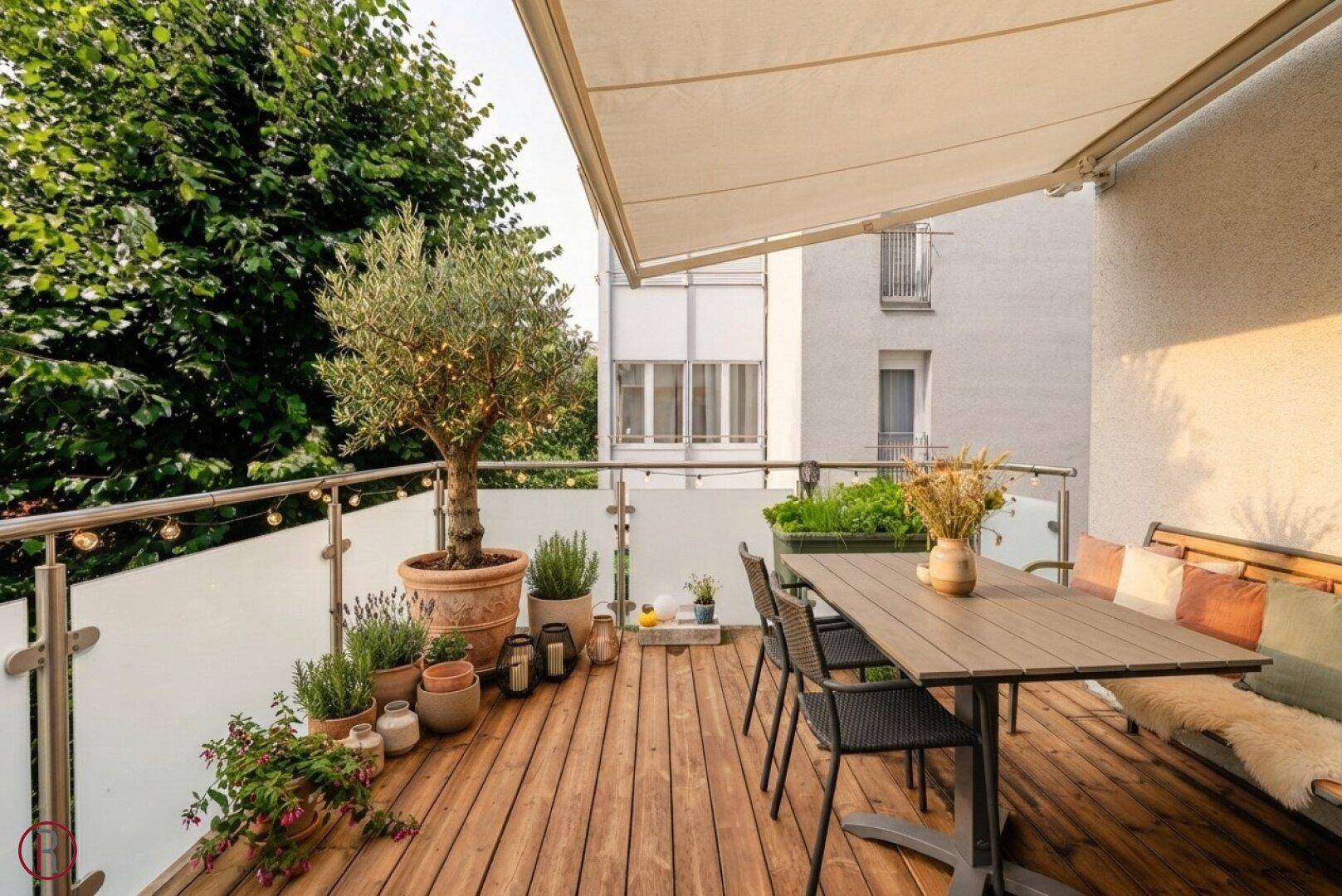 Gemütlicher Balkon mit Holzboden, Markise und Sitzgelegenheiten, umgeben von Grün und mit Blick auf die Umgebung.