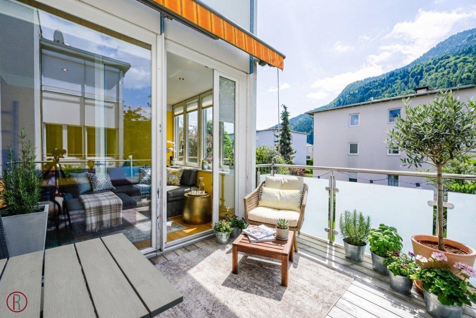 Sonniger Balkon mit Bergblick, Sitzgelegenheiten und Zugang zu einem verglasten Wintergarten.
