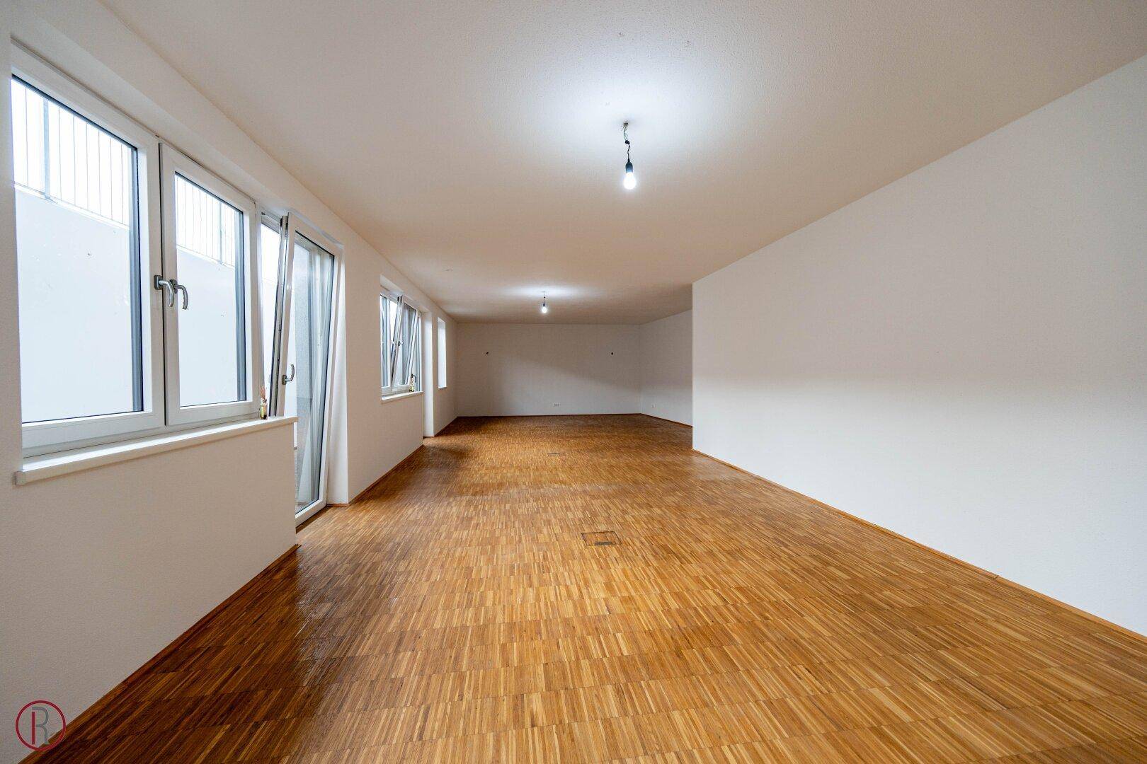 Leerer, heller Büroraum mit Holzboden und großen Fenstern, bereit für die individuelle Gestaltung.