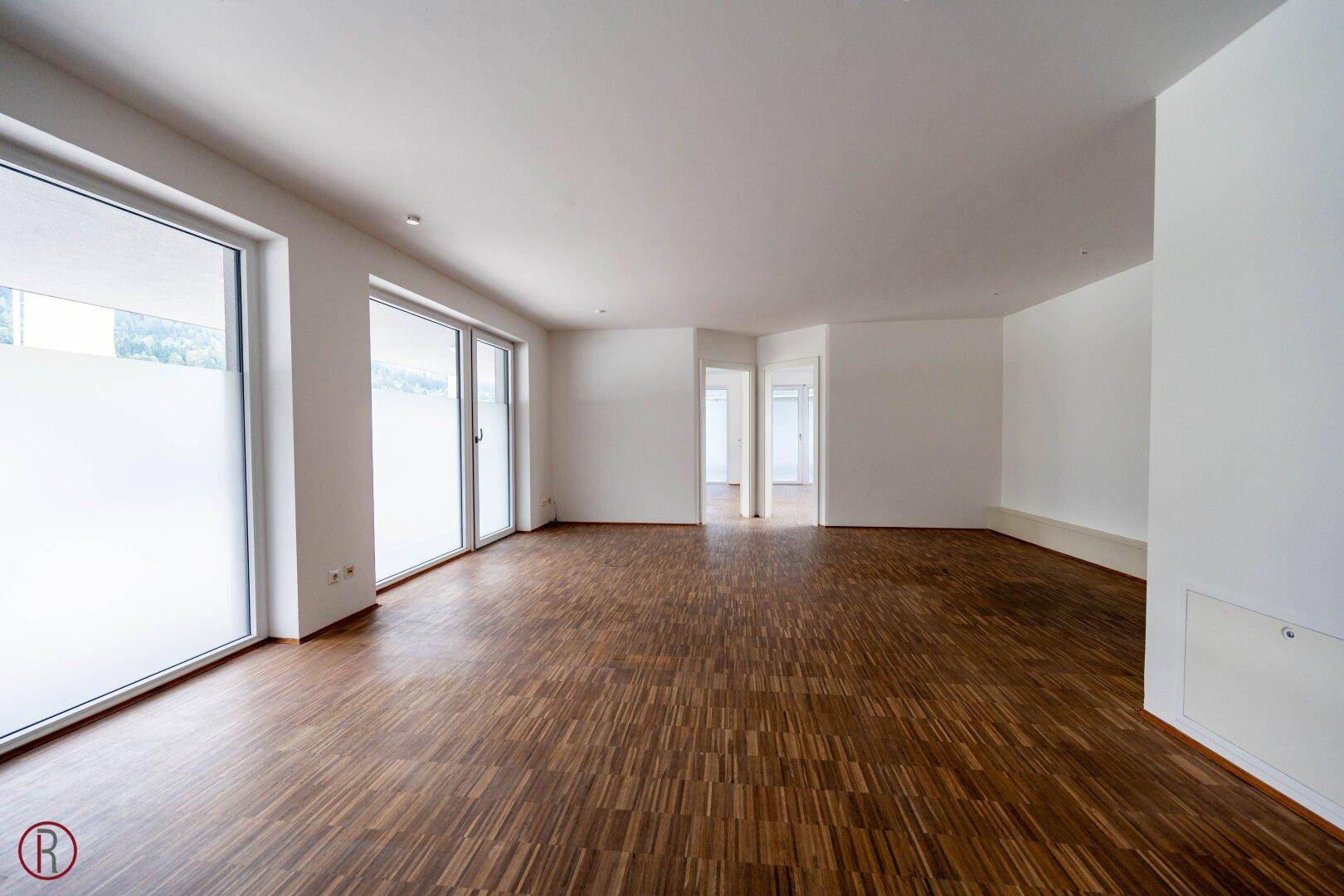 Großer, leerer Büroraum mit Holzboden und bodentiefen Fenstern, der vielseitig nutzbar ist.