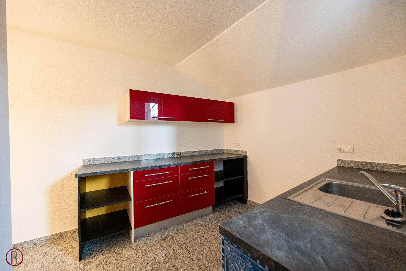 Kleine Küchenzeile mit roten Hochglanzschränken, Granitarbeitsplatte und Spüle in einem modernen Raum.