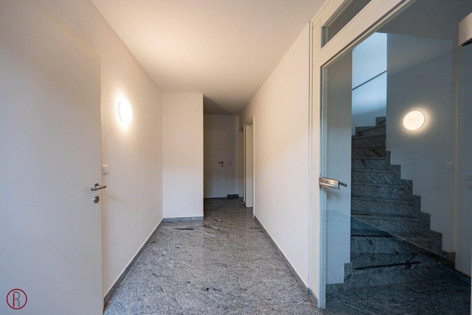 Heller Eingangsbereich mit Marmorboden und einer Treppe, die in die oberen Etagen führt.