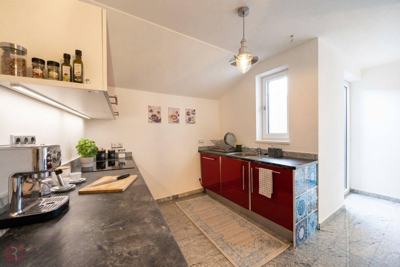 Funktionale Küchenzeile mit roten Schränken, Granitarbeitsplatte, Spüle und Fenster für Tageslicht.