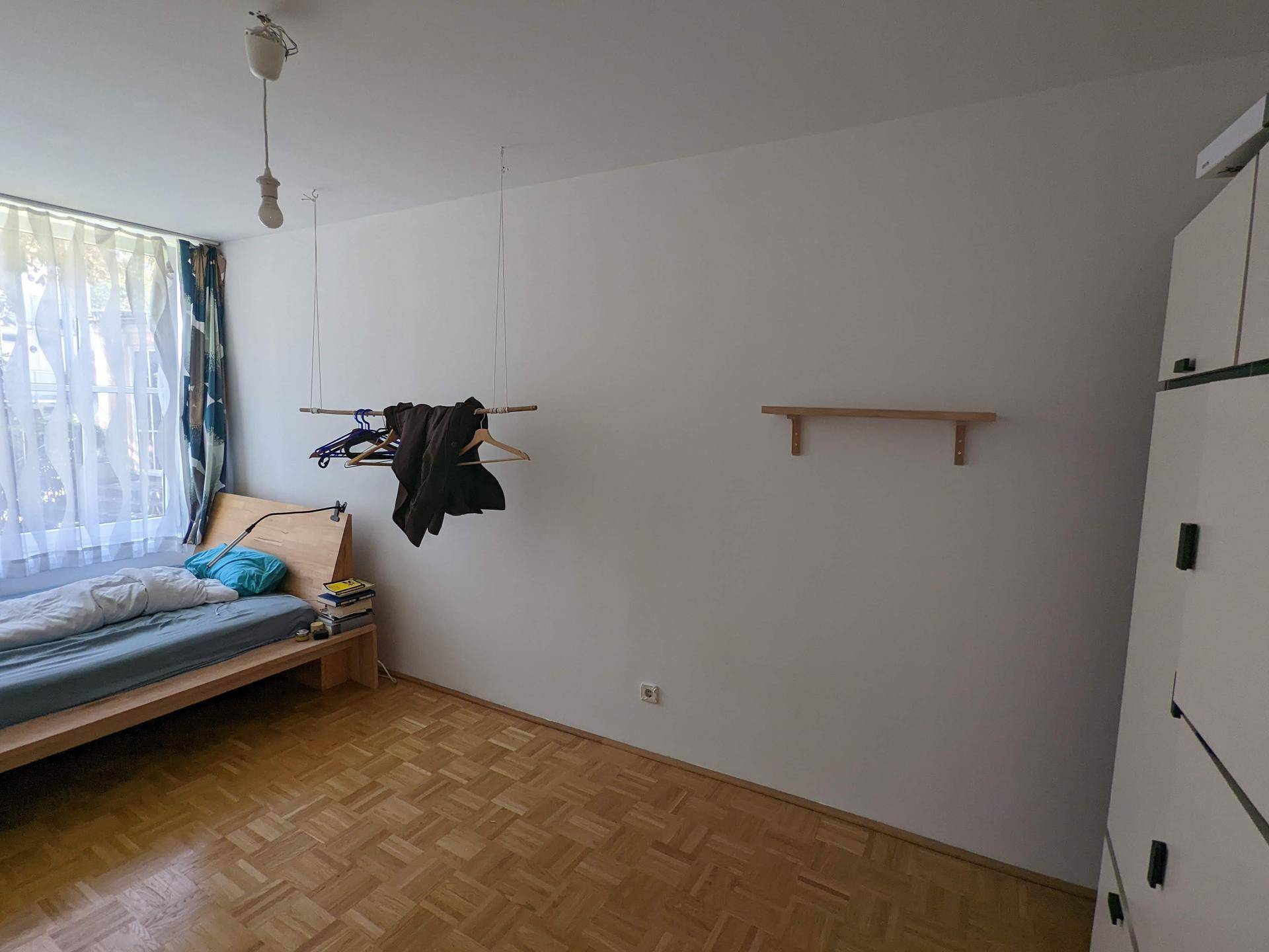 Schlafzimmer mit Holzbett, Parkettboden und einem Fenster, das viel natürliches Licht bietet.
