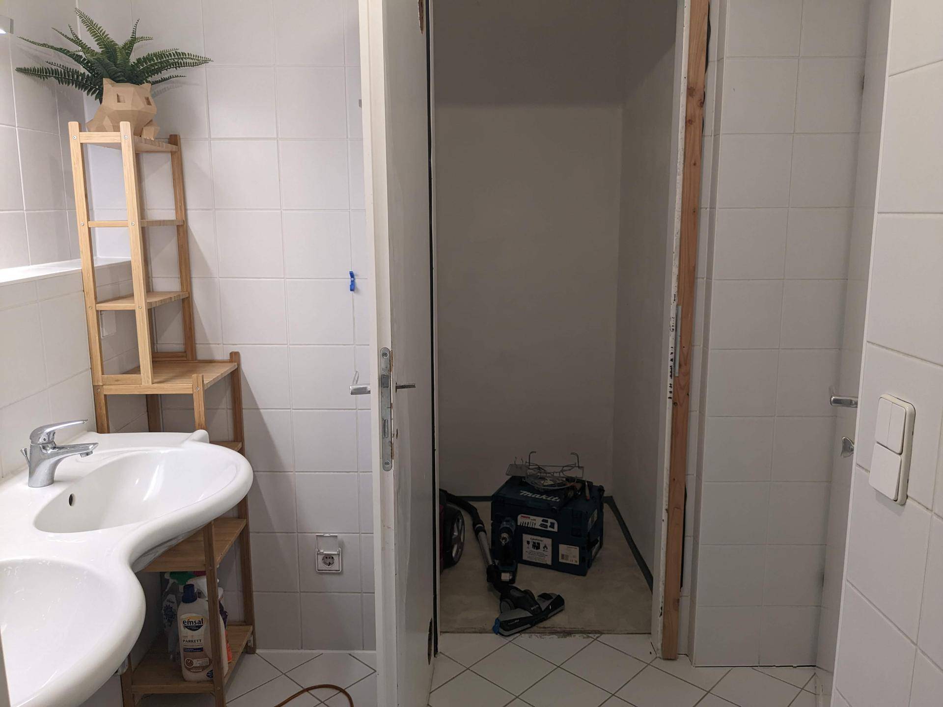 Helles Badezimmer mit Doppelwaschbecken, weißen Fliesen und Zugang zu einem Abstellraum.