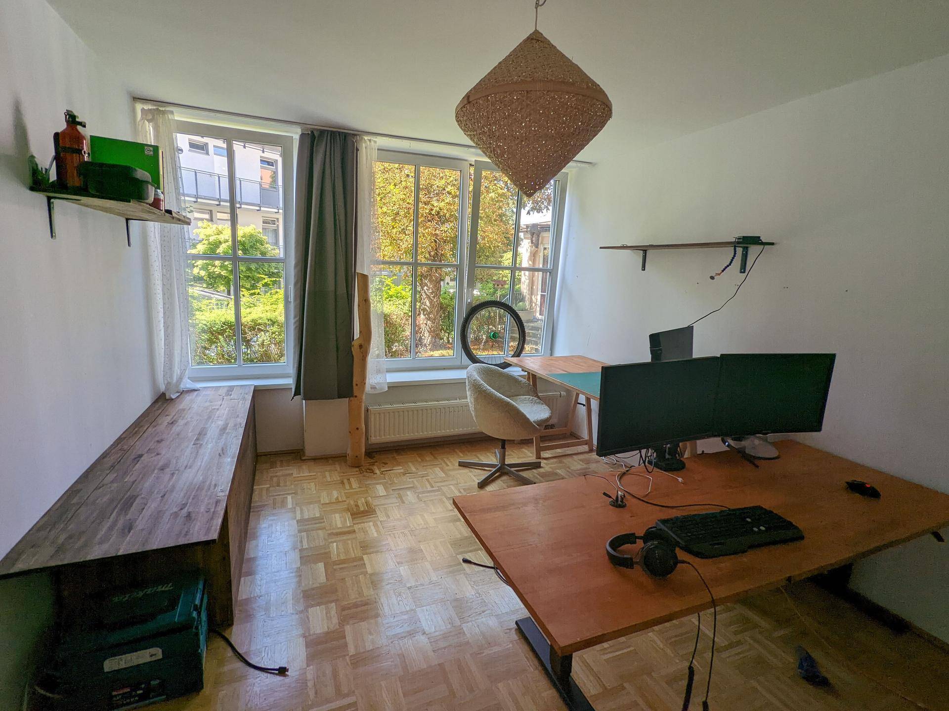 Helles Arbeitszimmer mit zwei Schreibtischen, Parkettboden und Blick ins Grüne durch große Fenster.
