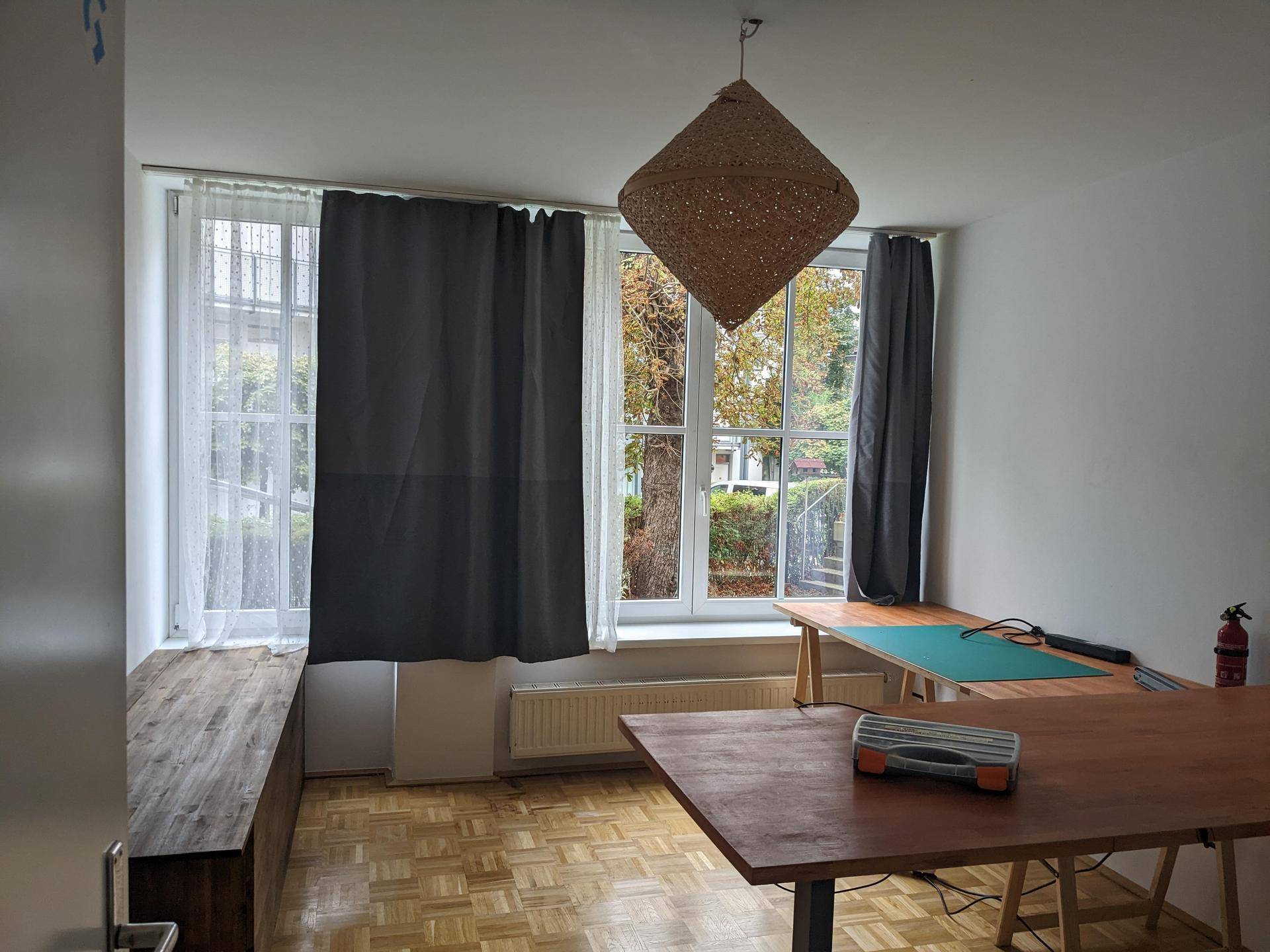Geräumiges Arbeitszimmer mit Holzboden, großen Fenstern und einer auffälligen Hängelampe.