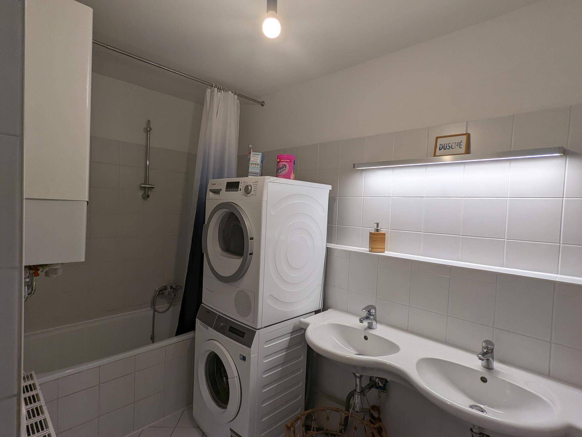 Badezimmer mit Badewanne, Doppelwaschbecken und gestapelter Waschmaschine und Trockner.