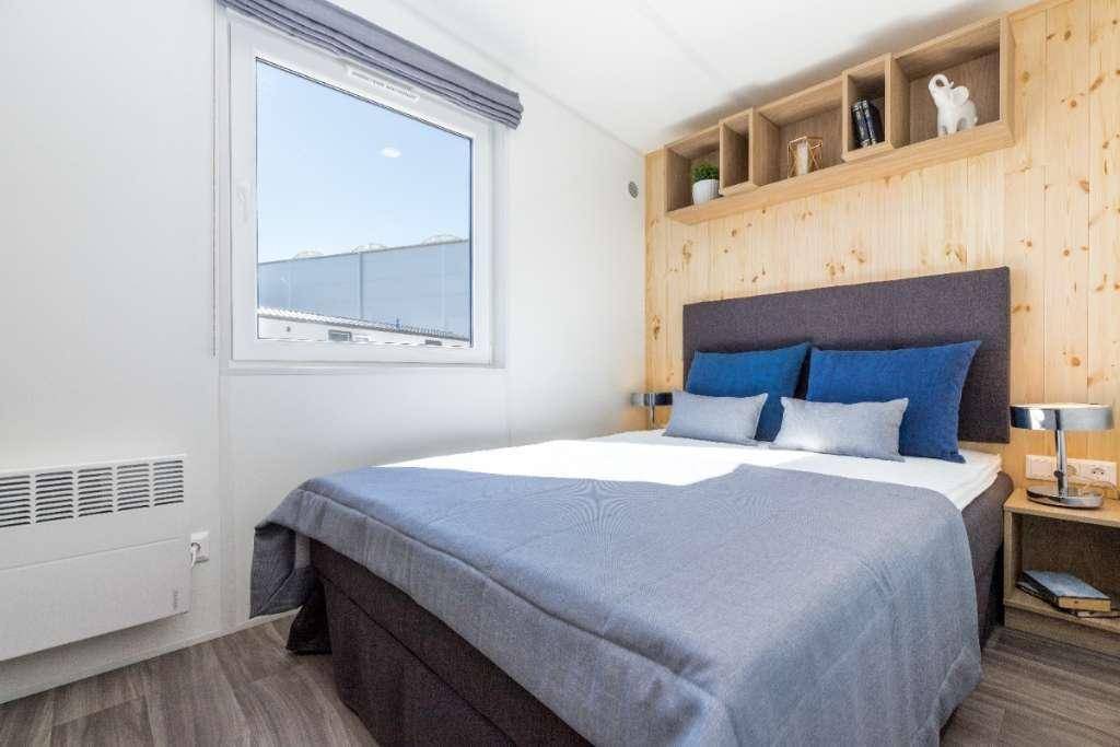 Gemütliches Schlafzimmer mit Doppelbett, Holzwandverkleidung und großem Fenster für Tageslicht.