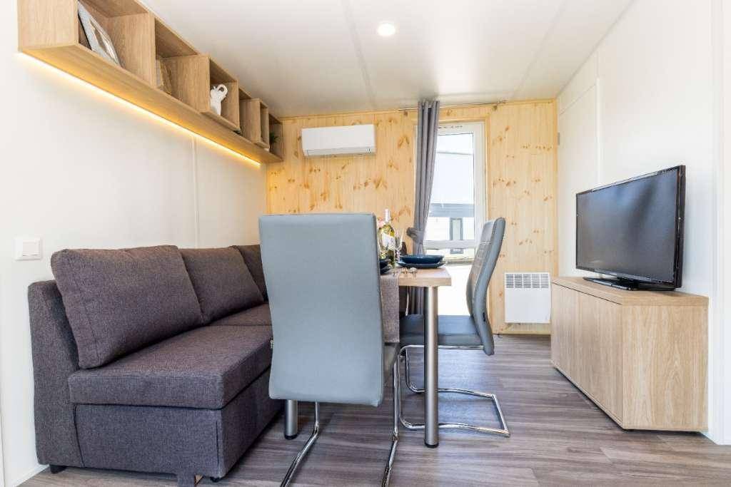 Heller Wohn- und Essbereich mit Sofa, Esstisch und Fernseher, ergänzt durch Holzelemente.