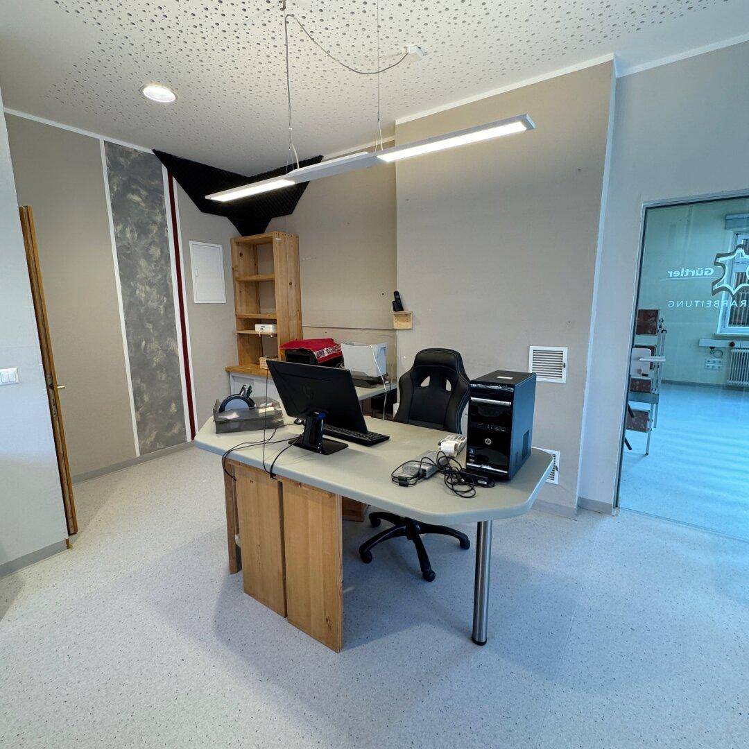 Arbeitsplatz in einem Büro mit Schreibtisch, Bürostuhl und Regalen an der Wand.