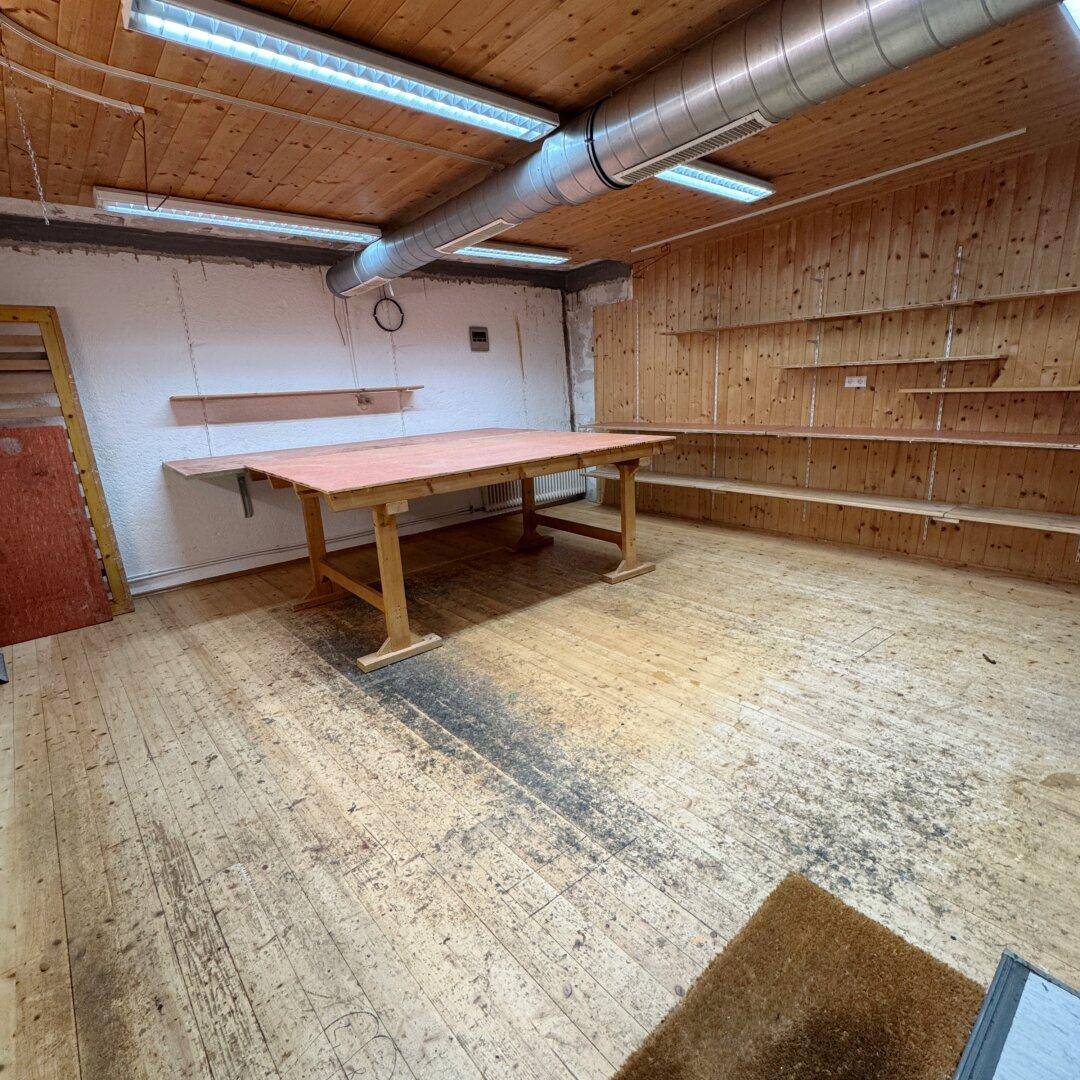 Werkstattraum mit Holzboden, Holzdecke, Regalen und einem großen Arbeitstisch.