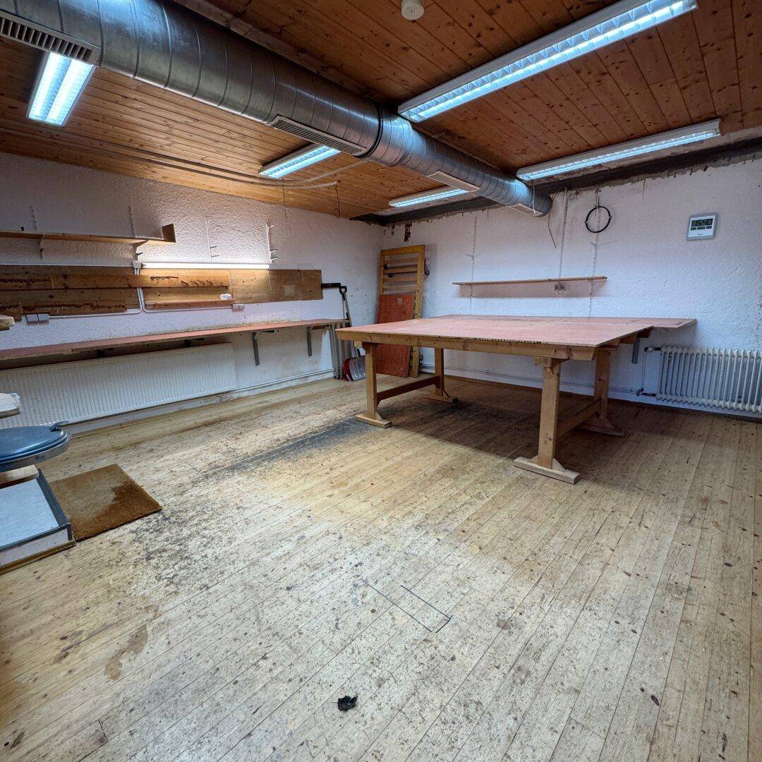 Geräumige Werkstatt mit Holzboden, Holzdecke und einem großen Arbeitstisch.