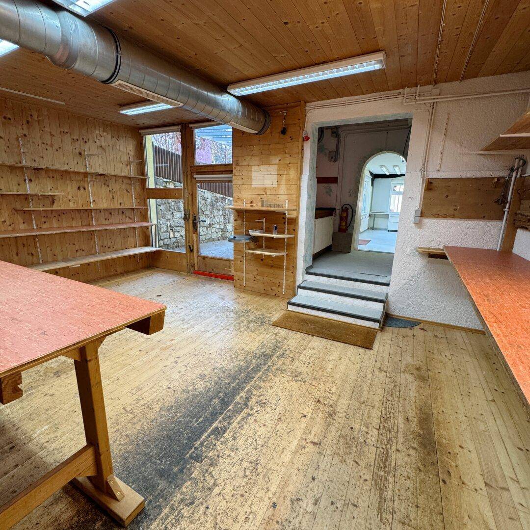 Werkstatt mit Holzboden, Holzdecke, Regalen und einem Ausgang zum Außenbereich.