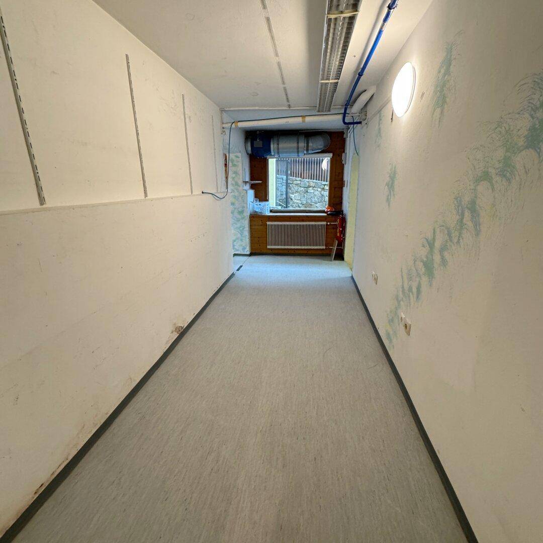 Schmaler Lagerraum mit Vinylboden, einem Fenster und einfacher Beleuchtung.