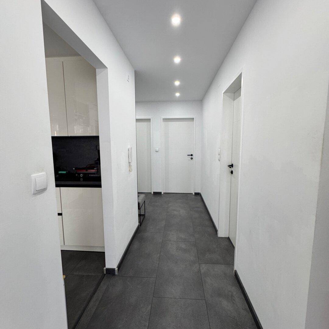 Langer, heller Flur mit dunklem Fliesenboden und Zugang zu verschiedenen Zimmern der Wohnung.